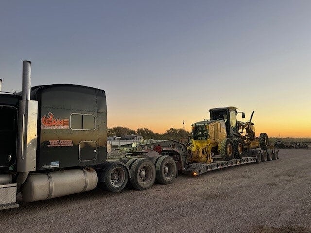 Game Heavy Hauling loading CAT motorgrader at sunset CAT motorgrader at sunset